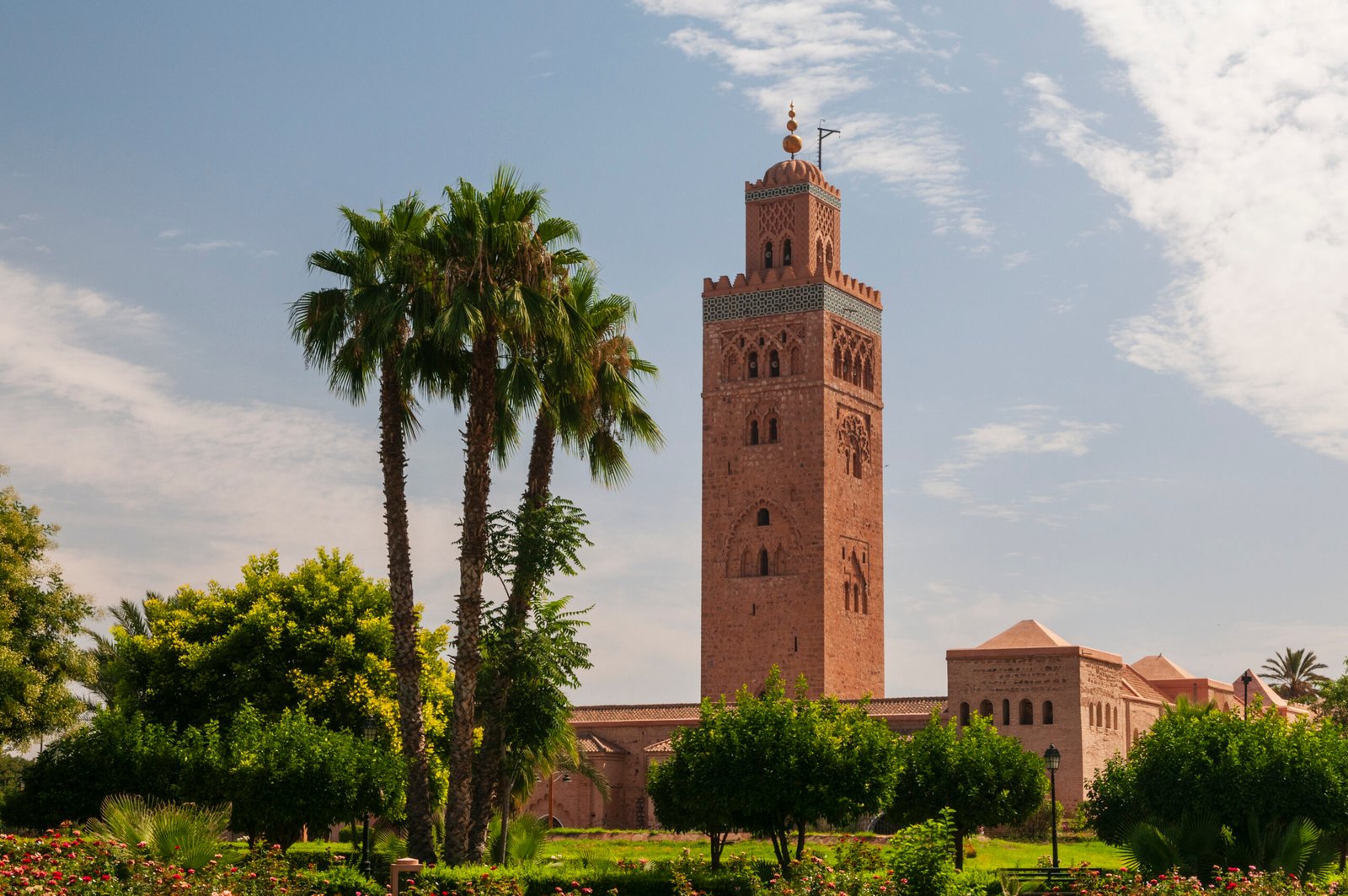 An iconic Moroccan minaret towers over lush gardens under a clear blue sky.